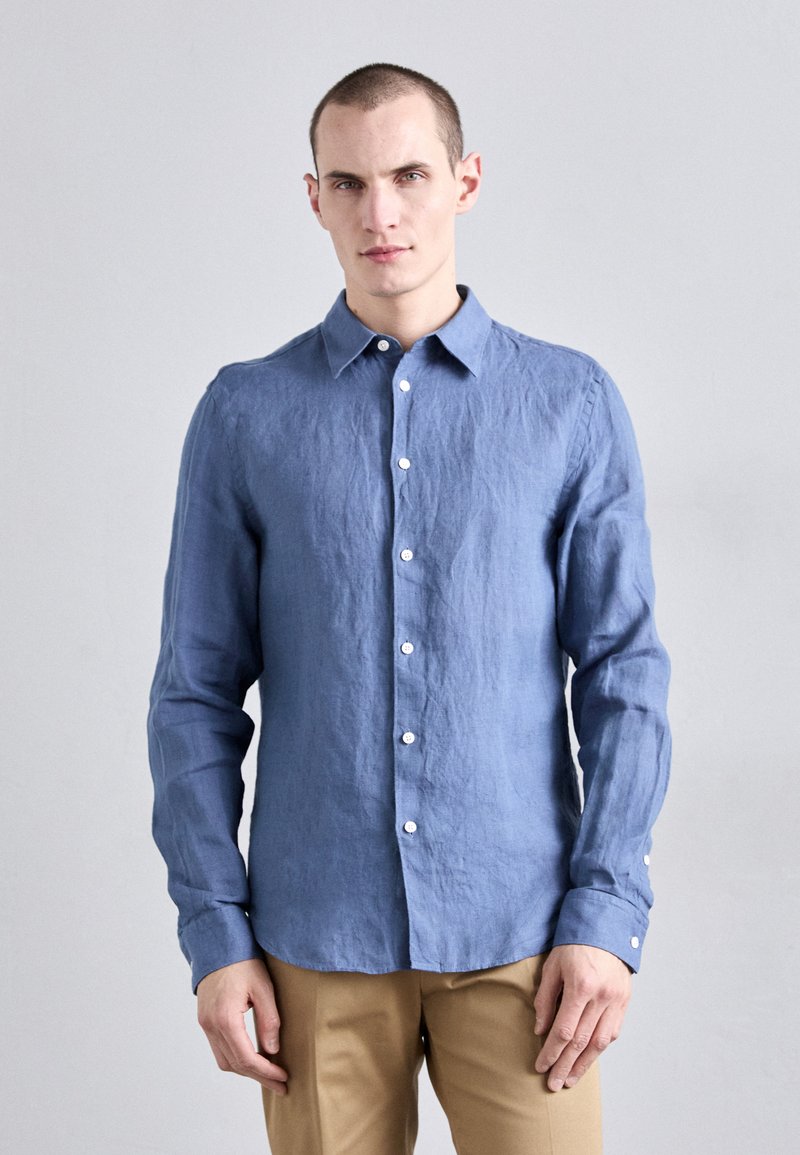 Camisa de lino de manga larga en azul claro, con cuello abotonado, cierre frontal con botones y botones blancos; acabado suave y texturizado.