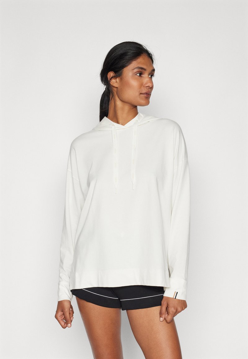 Vit hooded sweatshirt med långa ärmar, som har en avslappnad passform och dragsko, i kombination med svarta träningsshorts med vita accenter.