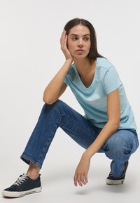 Jasnoniebieska koszulka z okrągłym dekoltem i subtelnym nadrukiem. Połączona z niebieskimi dżinsami i czarnymi trampkami, prezentując swobodny styl.