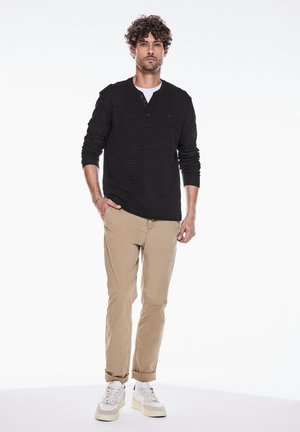 Sort langærmet henley-shirt med et tekstureret mønster, parret med khaki chinos og hvide sneakers, der viser en afslappet pasform.