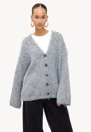 Grijze fuzzy cardigan met V-hals, grote knopen en brede mouwen, gecombineerd met zwarte wijde broek. Glad textuur en gezellige uitstraling.