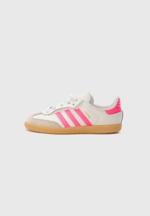 Hvid og beige sneaker med gummisål, pink striber, pink hælkappe, hvide snørebånd og gylden "SAMBA" tekst på siden.