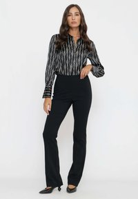 Pantaloni neri a gamba dritta abbinati a una blusa nera e bianca a fantasia con righe verticali e motivi a catena. Il materiale sembra setoso.