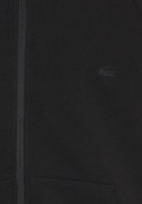 Sort zip-up hoodie lavet af blød bomuld, med en tekstureret stof, to forlommer og et diskret broderet logo på brystet.
