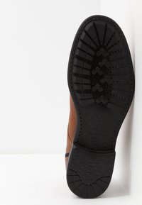 Brun läder sko med en kontrasterande svart gummisula. Sulan har ett strukturerat mönster för grepp och är märkt med varumärket "GEOX."