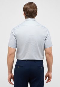 Kurzärmliges Button-Up-Hemd in hellblau mit dezentem Karomuster, kombiniert mit marineblauen Hosen mit Gesäßtaschen und einem Knopfdetail.