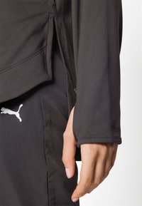 Svart långärmad sporttröja med tumhål. Mjuk, elastisk tyg med platta sömmar. Har en liten vit logotyp i botten.