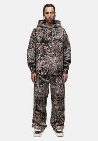 Set di felpa con cappuccio e pantaloni in marrone e verde, con un motivo a foglie. La felpa presenta una tasca frontale, mentre i pantaloni hanno un elastico in vita.