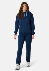 Felpa con cappuccio di colore blu navy con tasca anteriore e lacci, abbinata a pantaloni della tuta coordinati, entrambi in un tessuto texturizzato.
