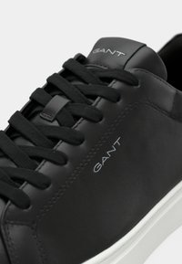 Adidași negri din piele cu șireturi negre, având un guler căptușit și o talpă din cauciuc alb. Branding-ul GANT subtil pe lateral.