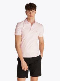 CAMISA POLO ROSA CLARO EM ALGODÃO, COM COLAR CLÁSSICO E UM PEQUENO LOGÓTIPO NO LADO ESQUERDO DO PEITO, ACOMPAHADA DE CALÇÕES PRETOS.