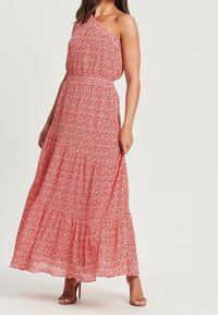 Robe maxi rouge à fleurs à une épaule, avec une taille cintrée, une jupe à volants et un tissu léger, présentant des motifs floraux blancs tout au long.