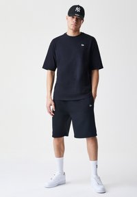 T-shirt nera in cotone a girocollo e pantaloni corti abbinati, con un piccolo logo sul lato sinistro del petto. Indossato con scarpe da ginnastica bianche e calzini.