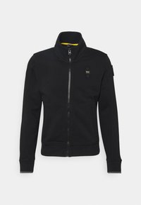 Svart zip-up jacka med hög krage, utrustad med en liten logopatch, sidofickor och ribbstickade ärmslut. Slät textur med en figurnära design.