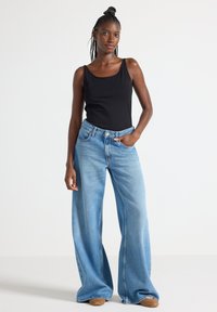 Sort tanktop parret med vidde lysblå jeans. Jeansene har høj talje og klassisk fem-lomme design. Neutralt fodtøj fuldender looket.