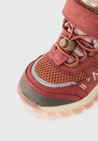 Chaussure de sport rouge et marron avec tige en maille, col rembourré et lacets élastiques. Dispose d'une semelle texturée et d'une semelle extérieure en caoutchouc partiellement transparente.