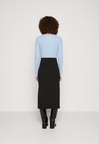Helles blaues, geripptes Langarmoberteil, kombiniert mit einem schwarzen Midirock. Der Rock hat einen Schlitz hinten und einen glatten Stoff, passend zu kniehohen schwarzen Stiefeln.