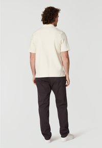 Ljusgrå kortärmad polo t-shirt, kombinerad med mörka byxor och vita sneakers, sedd bakifrån, vilket framhäver den stickade texturen och kragen.