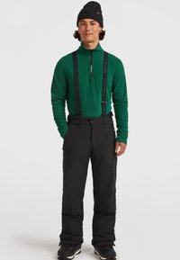 Groene fleece trui met ritssluiting, zwarte skibroek met bretels en een zwarte beanie. Textuurmaterialen; praktische ontwerp voor buitenkleding.