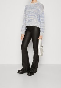 Lichtblauwe en witte gebreide trui met ribbelzoom, gecombineerd met aansluitende zwarte leren flarebroeken en een zilverkleurige handtas met versieringen. Zwarte plateauboots.