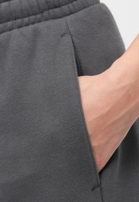 Szare dresy o miękkiej teksturze, z otwartą kieszenią, w której znajduje się ręka, oraz elastycznym paskiem dla komfortu.