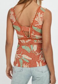 Tank top w kwiatowym wzorze w odcieniach rdzy i kremu z zielonymi akcentami. Posiada niski tył i dekoracyjny pasek na ramionach.