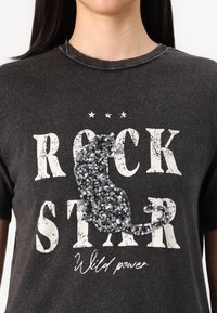 Tumehall T-särk, millel on julge valge "ROCK STAR" tekst, musta sädelusega kassi kujutis ja kulunud detailid. Pehme kangas ning ümar kaelus.
