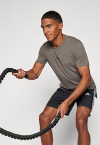 Gray athletic t-shirt with short sleeves and black logo, paired with black shorts featuring white stripes, gripping a thick black rope.
