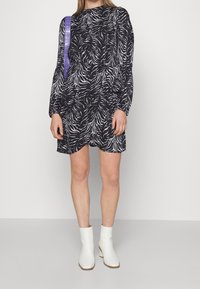 Černo-bílá šaty se zebrovým vzorem, dlouhými rukávy, řaseným pasem a vysokým výstřihem. Spárováno s bílými kotníkovými botami.