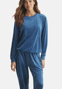 Twee-delige lounge-outfit set in zacht blauwe velvet. Het bovenstuk heeft een ronde hals en lange mouwen; de broek heeft een elastische tailleband en een losse pasvorm.