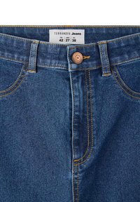Jeans in denim blu scuro con cuciture arancioni, chiusura a bottone e un'etichetta che indica le taglie 42 (ITA), 27 (USA) e 38 (UE).