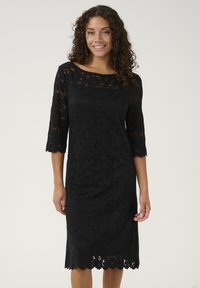 Black lace dress featuring three-quarter sleeves, floral pattern, scalloped hem, and a boat neckline. Smooth texture with intricate detailing.