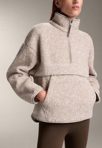 Beige fleece pullover met een halve rits, een voorknopzak en een oversized pasvorm. Beschikt over een zachte, getextureerde oppervlakte en contrasterende afwerking.