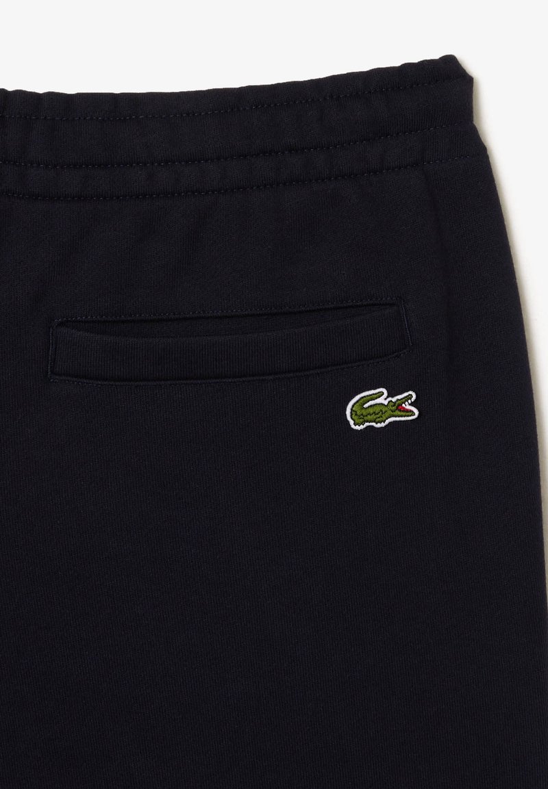 Pantalons de sudation marine en tissu doux, dotés d'une poche arrière et d'un petit logo de crocodile brodé en vert et blanc au dos.