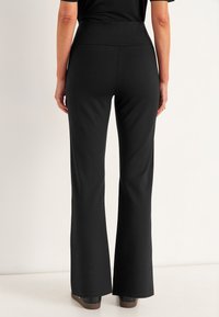 Schwarze, ausgestellte Hose mit glatter Stofftextur, hoher Taille und einer figurbetonten Silhouette, die bis zu einem weiten Bein reicht. Keine sichtbaren Verzierungen.