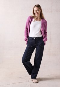 Rosa stickad kofta, vit topp och mörkblå vida jeans. Rosa knappar på koftan, subtila sömmar på jeansen och beige skor.