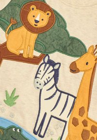 T-shirt ricamato con un leone, una zebra e una giraffa su uno sfondo chiaro, con dettagli di alberi verdi e acqua blu.