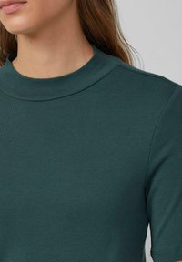 Tealowy, prążkowany top z wysokim dekoltem i krótkimi rękawami. Miękki, elastyczny materiał. Minimalistyczny design, gładka textura bez widocznych wzorów czy elementów metalowych.