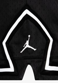 Zwarte basketbalschoenen met een gestructureerde stof, witte accenten langs de zijkanten en een wit Jumpman-logo aan de voorkant.