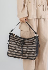 Svart och beige vävd axelväska med en strukturerad form, med en toppdragkedja, detaljer i form av kvast och en logotypaccent på framsidan.