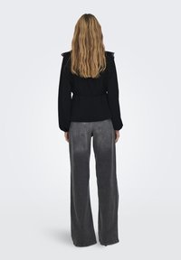 Sorte bluse med blonde-detaljer på skuldrene, kombinert med høytlivs, vide grå jeans. Modell sett fra baksiden.
