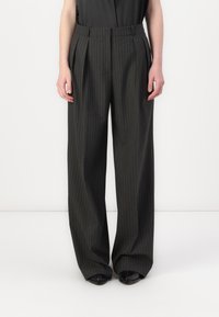 Brede broek van donker materiaal met verticale strepen. Heeft plooien bij de tailleband en een soepele textuur. Zwarte schoenen maken de look compleet.