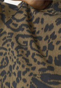 Dyreprintstof med en beige baggrund og mørkeblå leopardlignende mønstre. Teksturen virker glat og let elastisk.