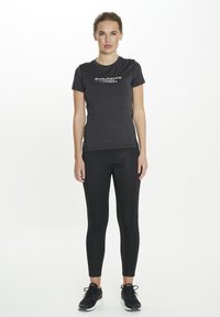 T-shirt de sport noir à évacuation de l'humidité avec le logo "ENDURANCE" en blanc, associé à un legging noir et des chaussures de sport noires. Texture lisse.
