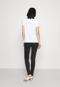 Camiseta blanca de manga corta combinada con jeans negros ajustados. La modelo lleva sandalias de tacón blanco y abiertas. Colores sólidos, ajuste casual.