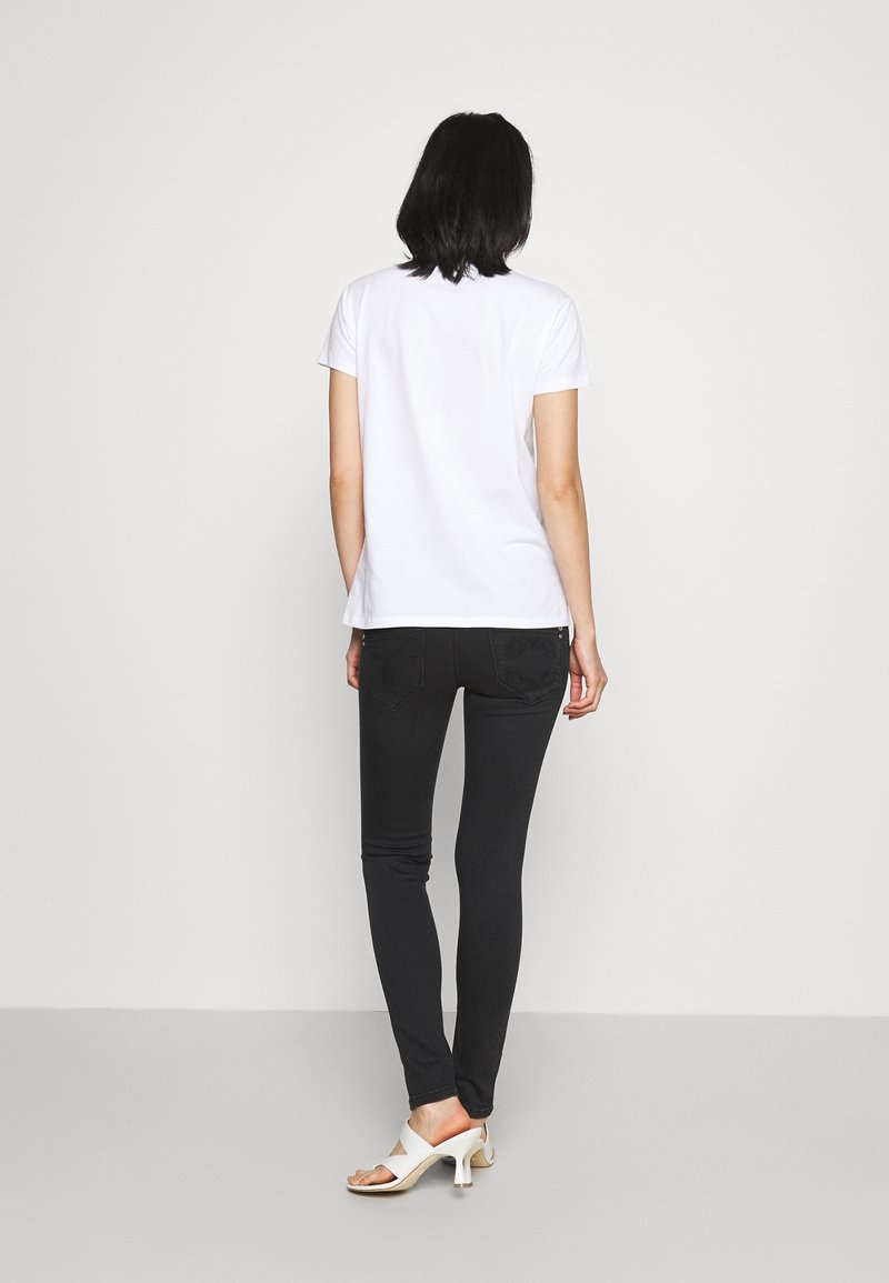 Camiseta blanca de manga corta combinada con jeans negros ajustados. La modelo lleva sandalias de tacón blanco y abiertas. Colores sólidos, ajuste casual.