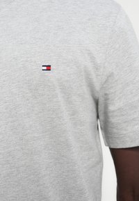 Γκρι βαμβακερό t-shirt με μικρό κεντητό λογότυπο σε μπλε, λευκό και κόκκινο χρώμα στην αριστερή πλευρά του στήθους. Κοντά μανίκια και στρογγυλή λαιμόκοψη.