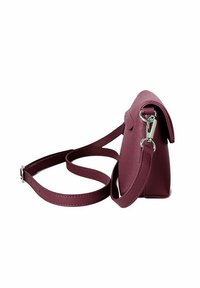 Malá texturovaná tmavě růžová kožená crossbody taška s klopou a nastavitelným popruhem ležící stočená na bílém pozadí.