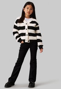 Schwarz-weiß gestreifter Strickcardigan mit ribbeliger Textur, V-Ausschnitt, Knöpfen vorne und schwarzen, figurbetonten Hosen.