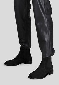 Stivaletti alla caviglia in suede nero con pannelli elastici laterali e un design elegante. La suola è nera lucida, con una silhouette minimalista e moderna.